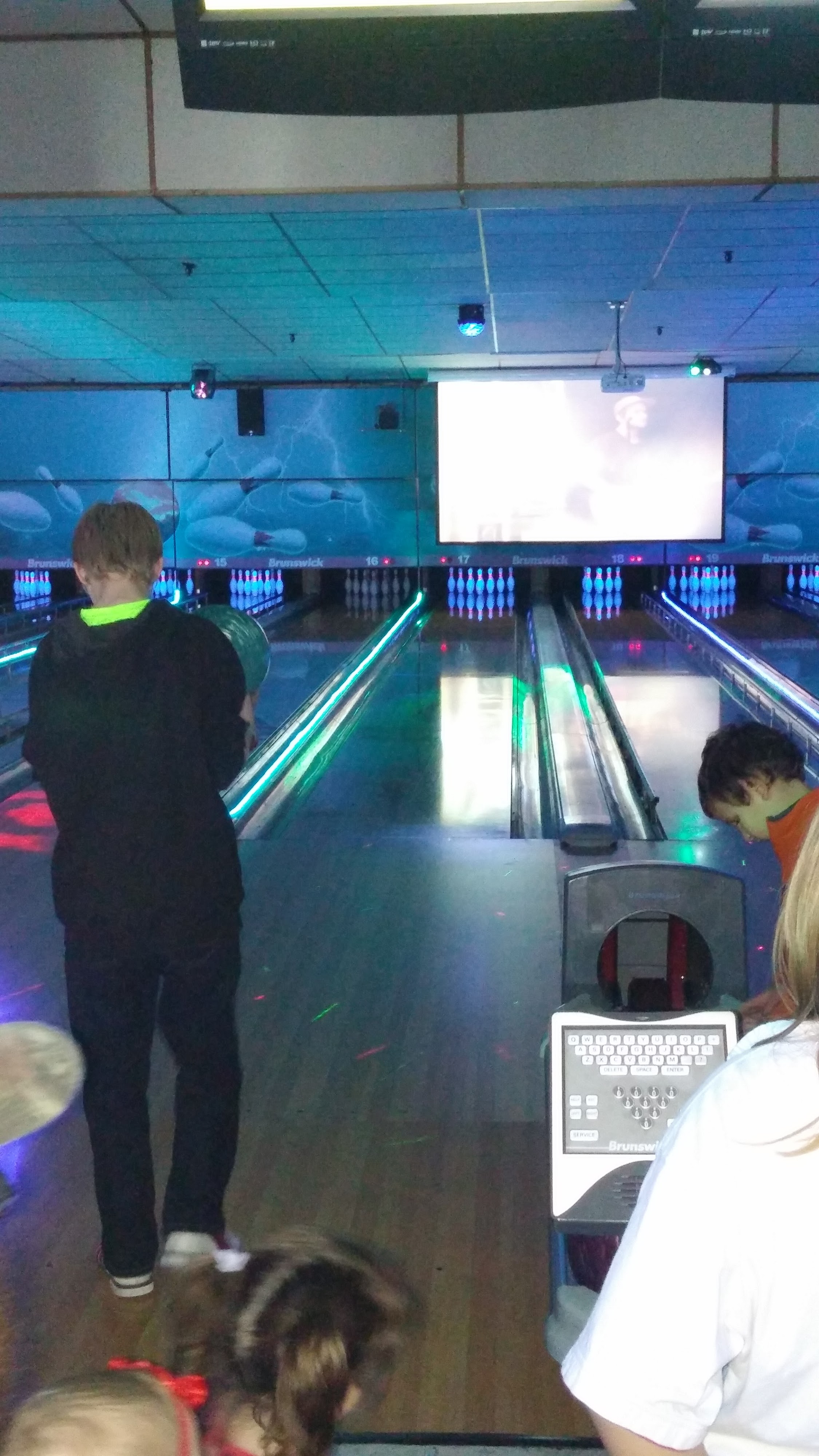 Several people bowling in a cosmic bowling setting with glowing pins and lanes.