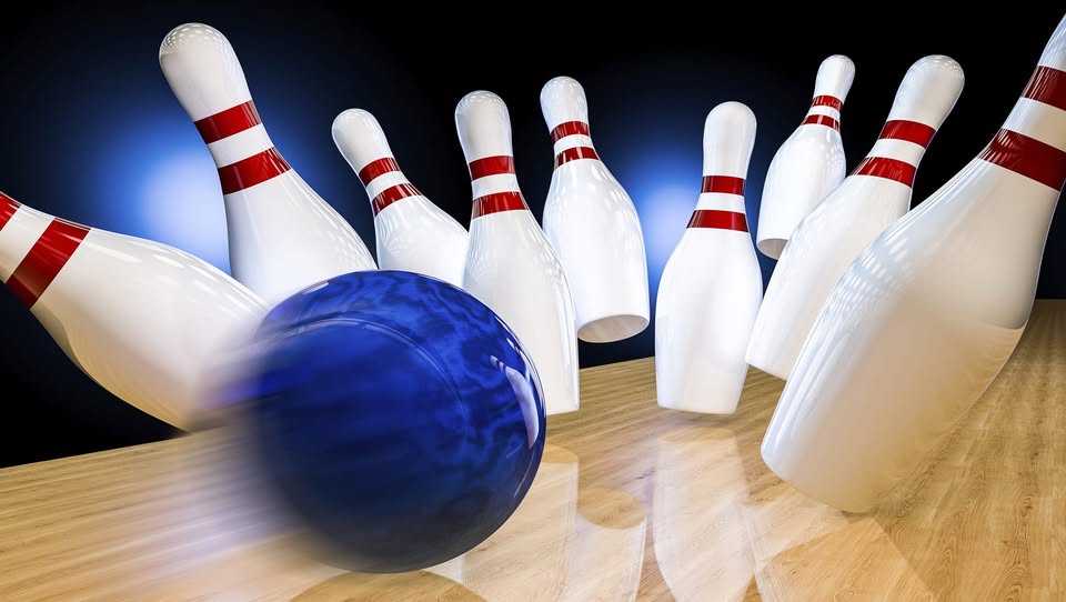 A blue bowling ball hitting white pins with red stripes on a wooden lane in a strike action shot.
