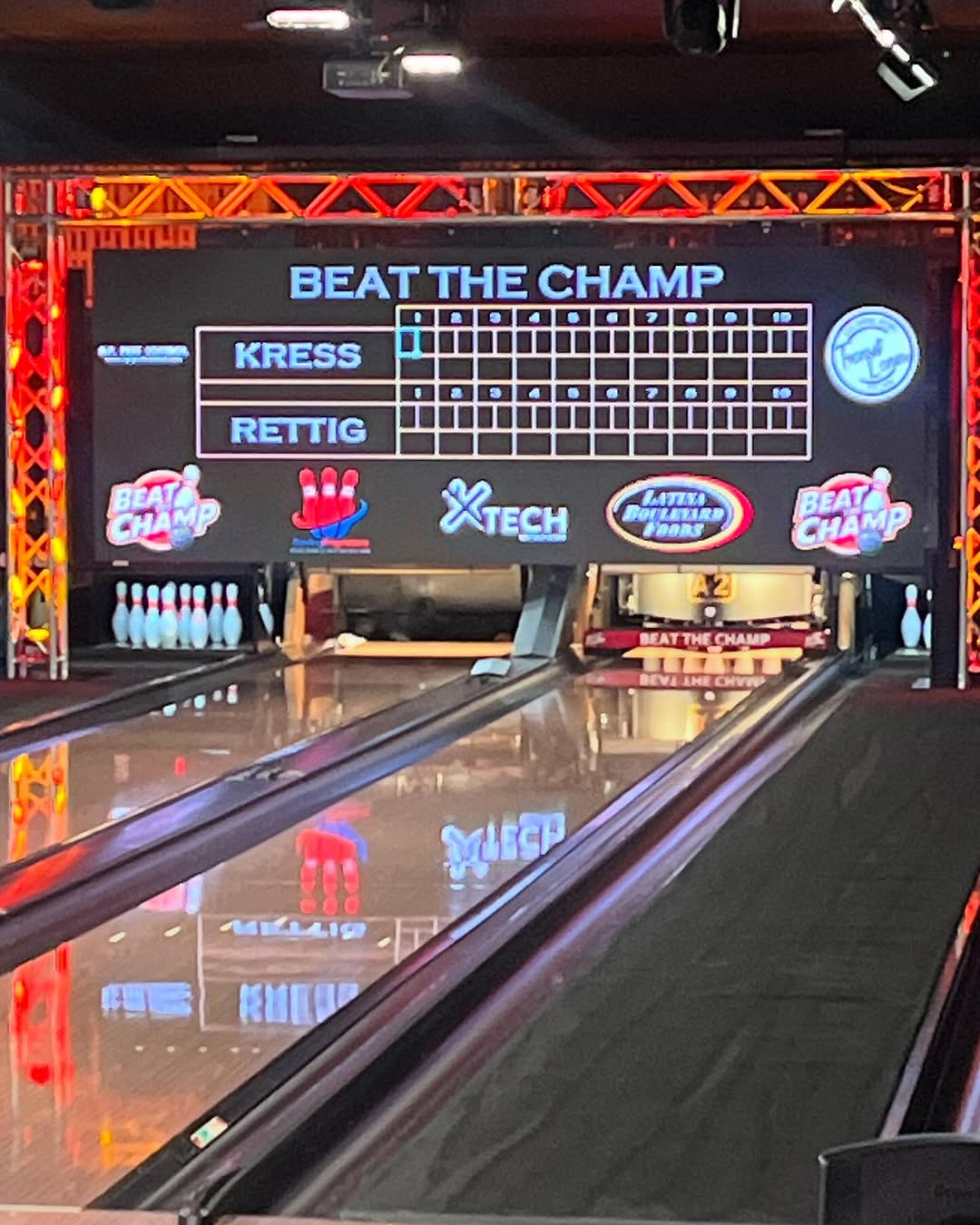 A digital bowling scoreboard at the end of a lane displaying a Beat the Champ match between two players.