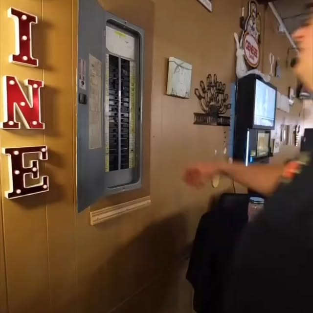 An open electrical panel on a wood-paneled wall next to illuminated marquee letters and bowling decor.