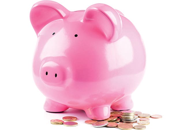 A shiny pink ceramic piggy bank standing next to a small pile of coins on a plain white background.