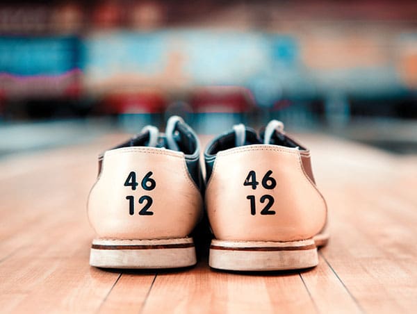 Close-up of the heels of two rental bowling shoes on a wooden floor with a blurred background.