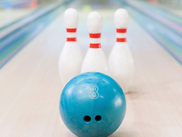 A light blue number 8 bowling ball on a lane with three bowling pins in the blurred background.