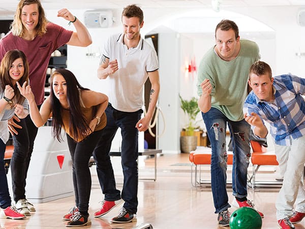 A group of diverse young adults cheering and bowling together on bright, polished lanes.