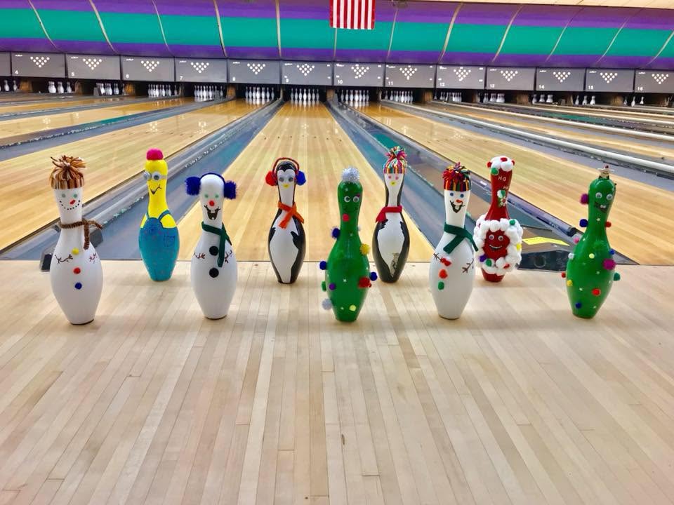 Nine bowling pins decorated as holiday characters like snowmen and penguins stand in a row on the bowling lanes.