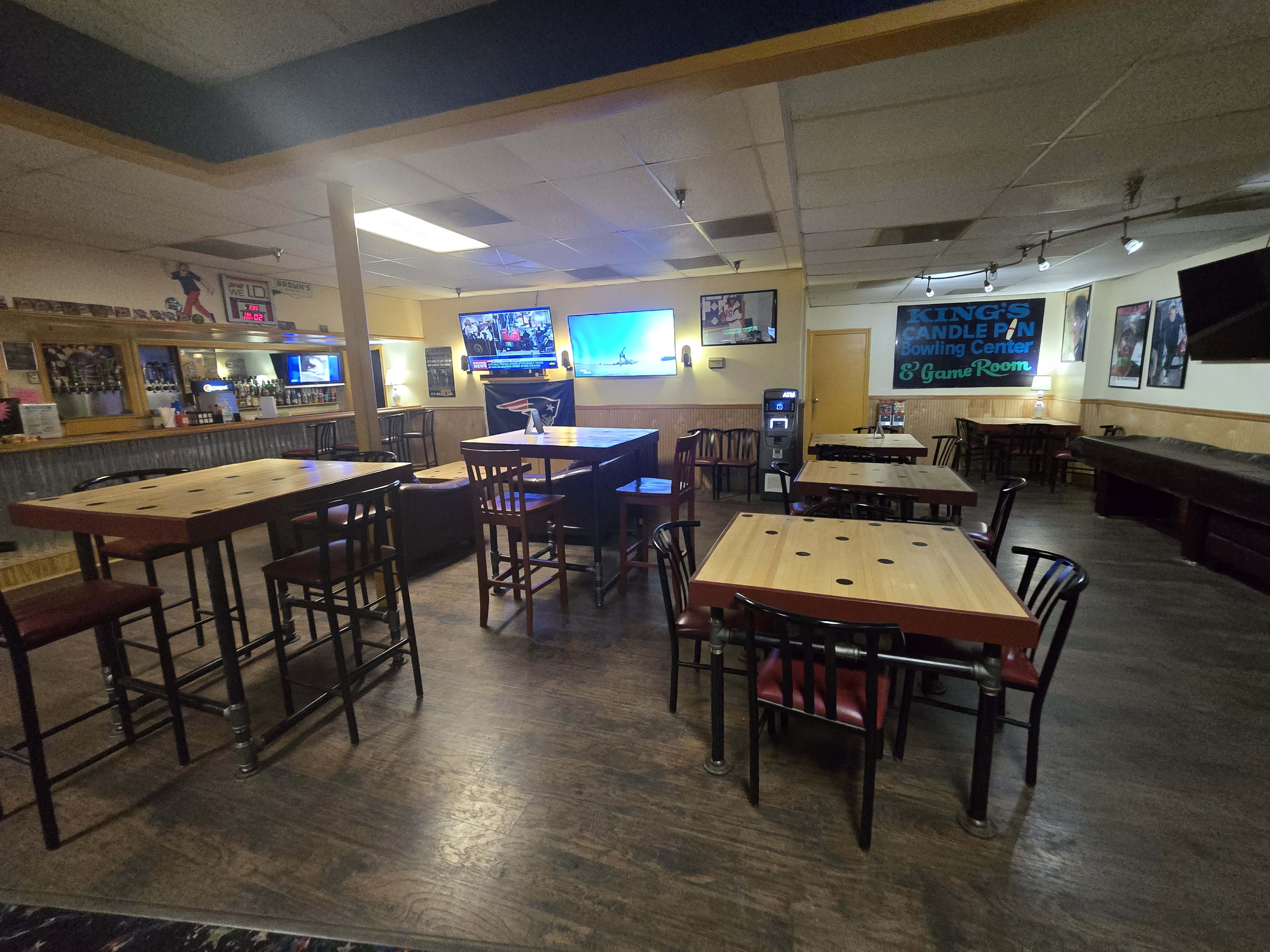 A bar and lounge area with wood-grain tables, bar stools, and several wall-mounted televisions showing sports.