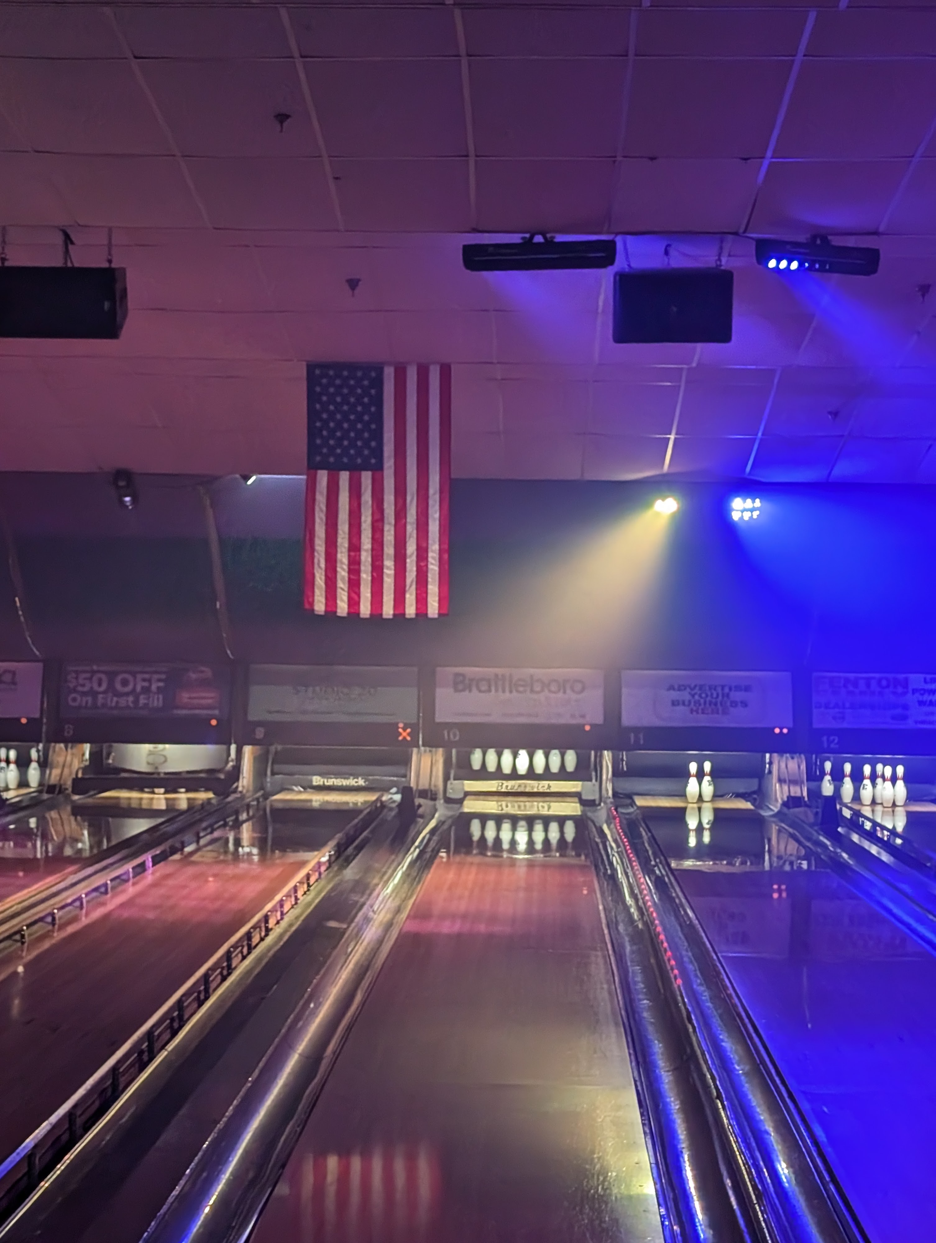 Bowling lanes under purple cosmic lighting with an American flag hanging above the pin deck.