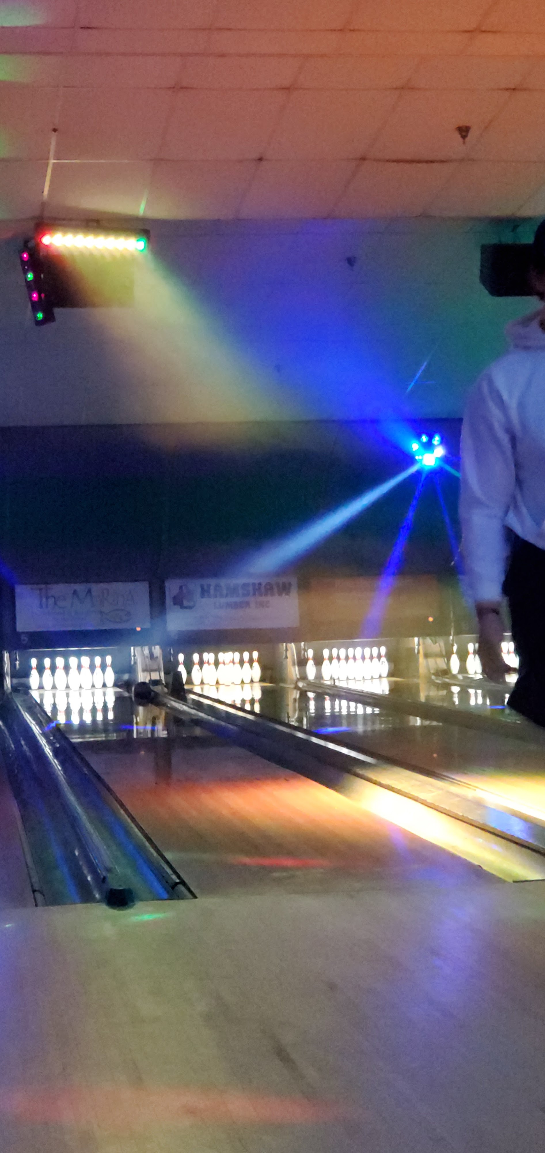 A bowling alley with colorful cosmic lights shining over the lanes and pins.