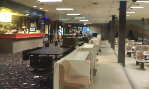 Indoor view of a bowling alley concourse featuring seating, ball returns, a service counter, and a pool table.