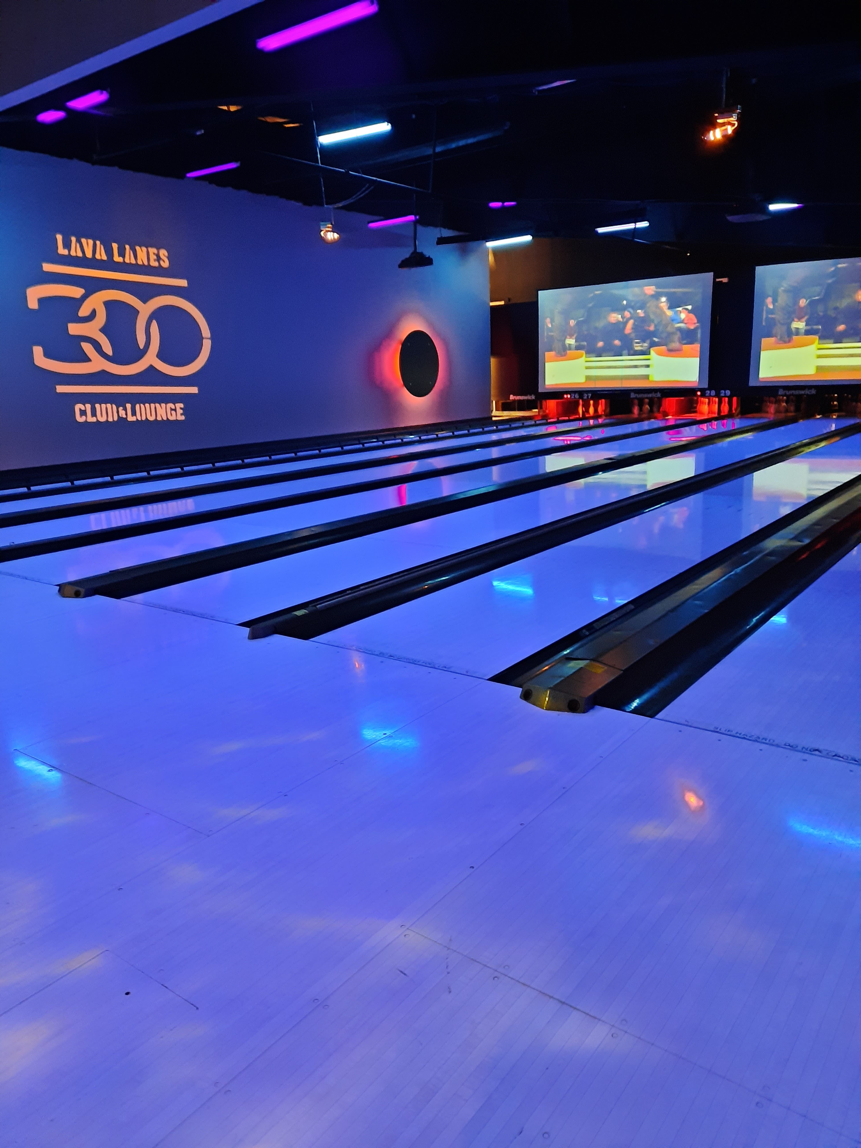 Bowling lanes at Lava Lanes Bend illuminated by blue neon lights with the 300 Club logo on the side wall.