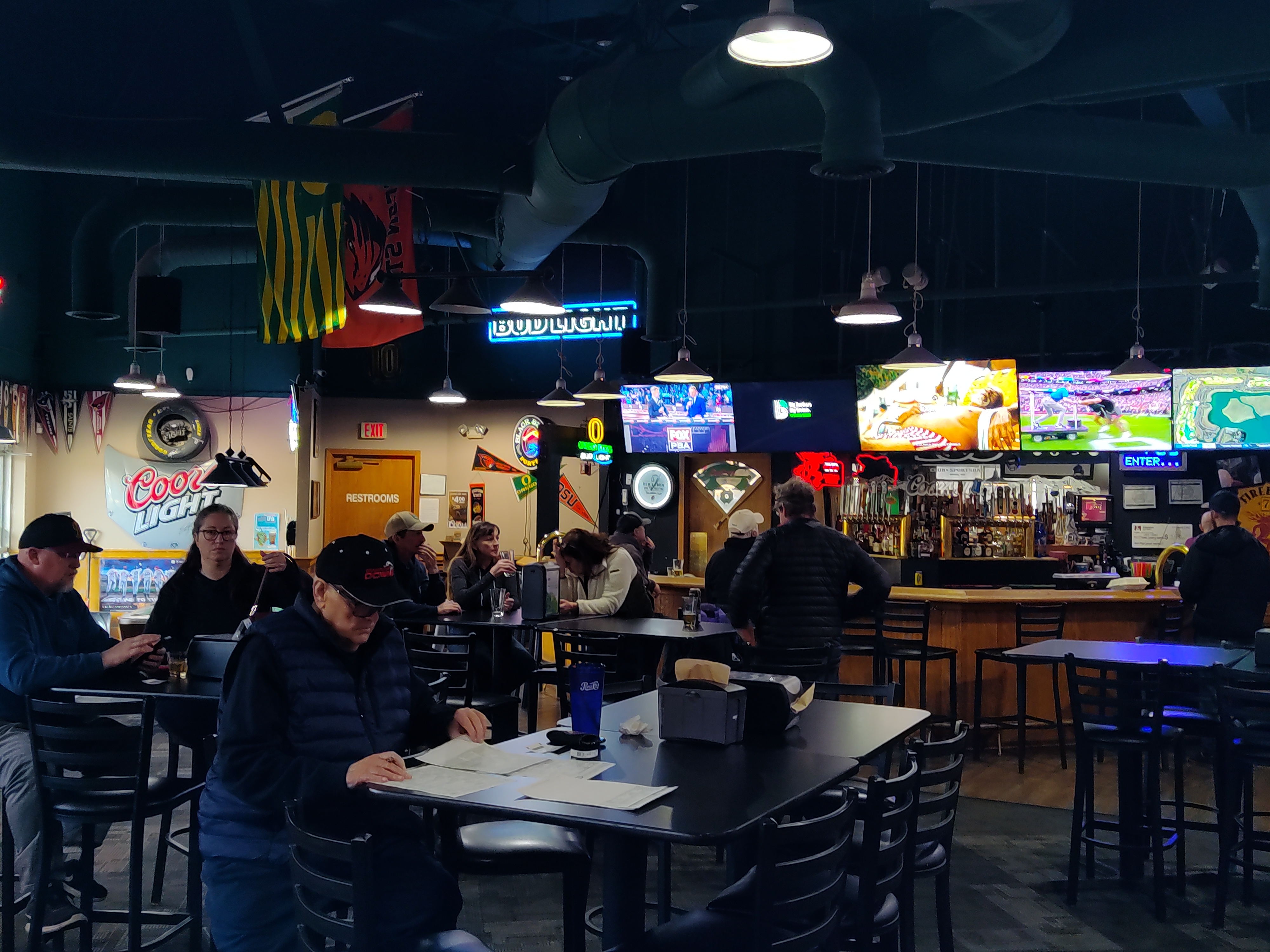 Interior view of a sports bar with patrons at tables and multiple television screens showing games.