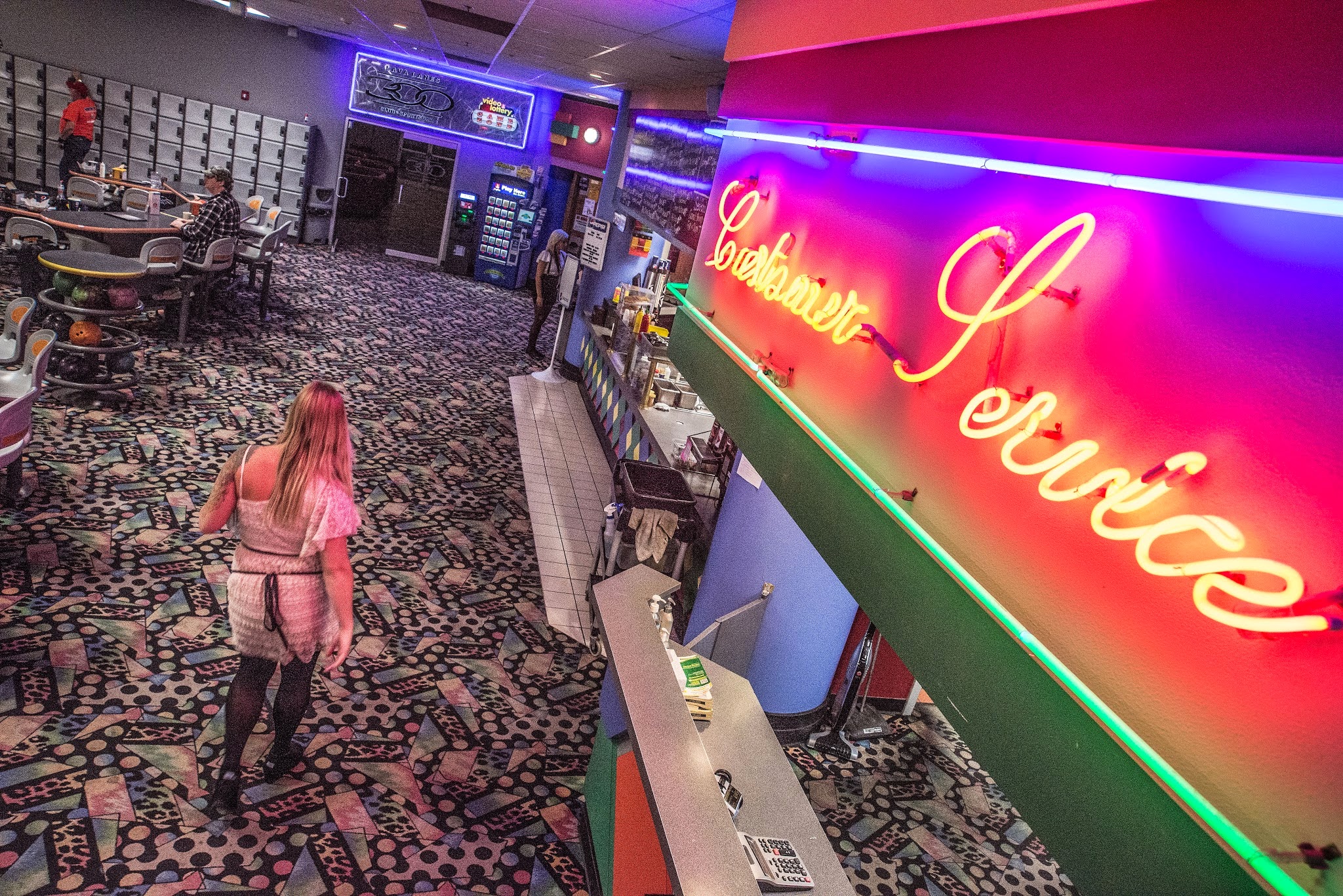 A glowing neon Customer Service sign overlooks a snack bar and patterned carpet in a bowling center.