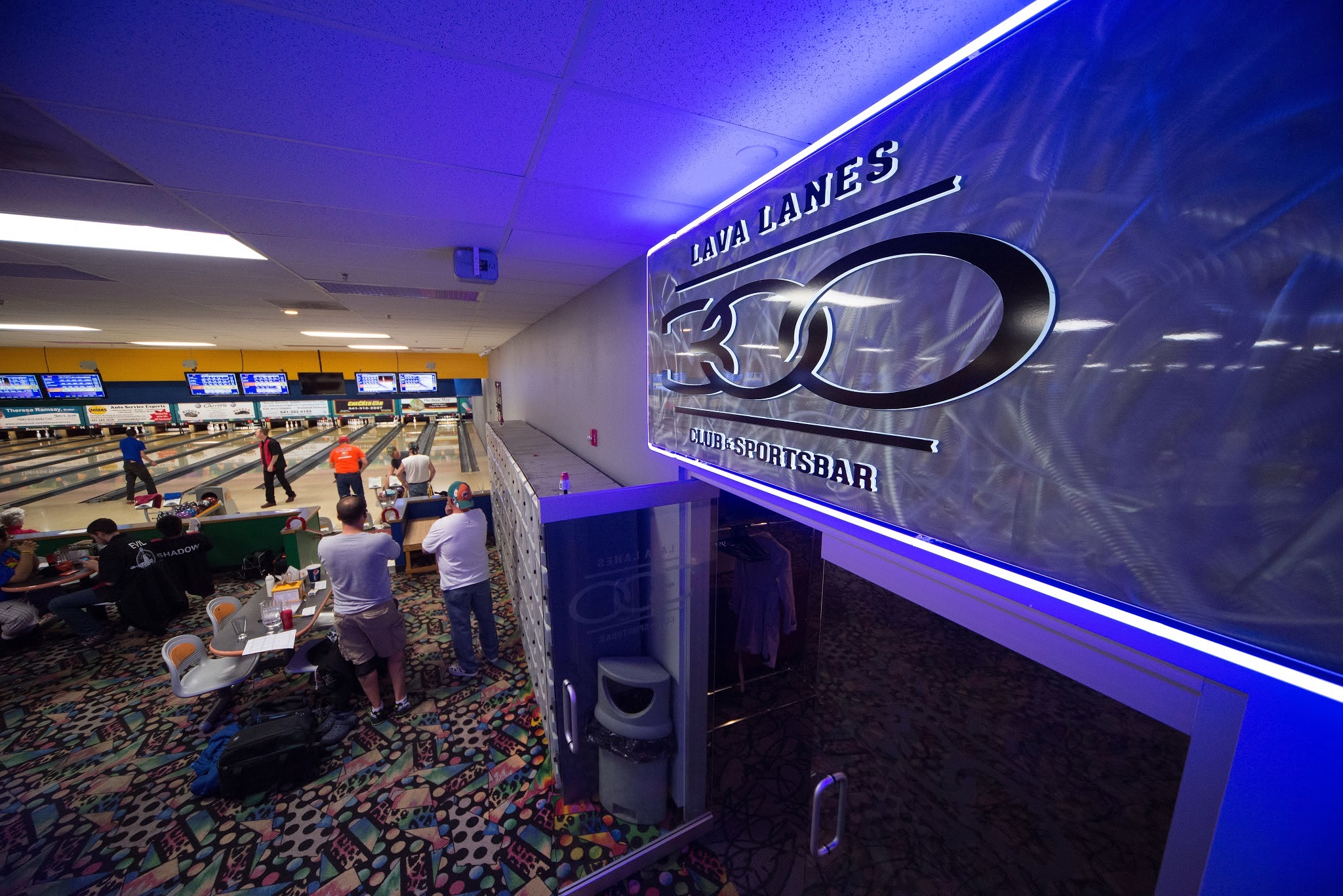 A large blue neon 300 Club and Sports Bar sign overlooks a busy bowling alley with people playing in the distance.