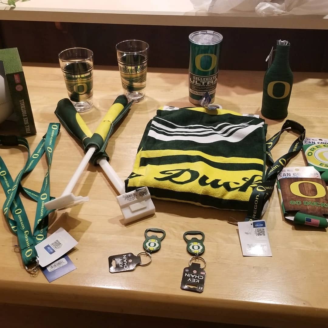 An assortment of Oregon Ducks branded gear including lanyards, glassware, and a towel on a wooden surface.