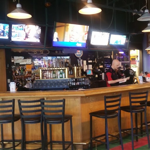 A sports bar with wooden counters, black stools, and several overhead televisions displaying different broadcasts.
