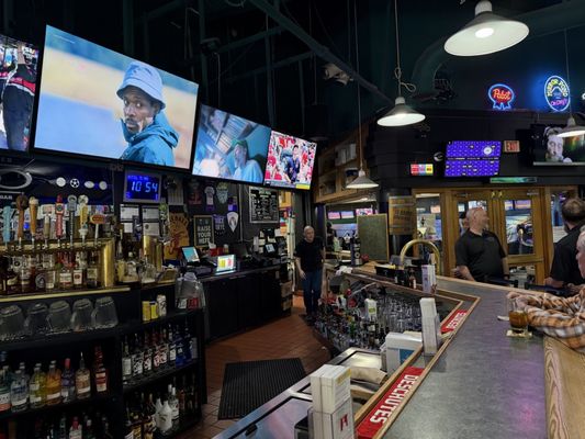 A sports bar with large televisions, beer taps, and a counter with patrons at Lava Lanes Bend.