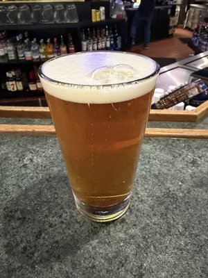 A full pint of amber beer with a frothy white head sitting on a dark stone bar counter.