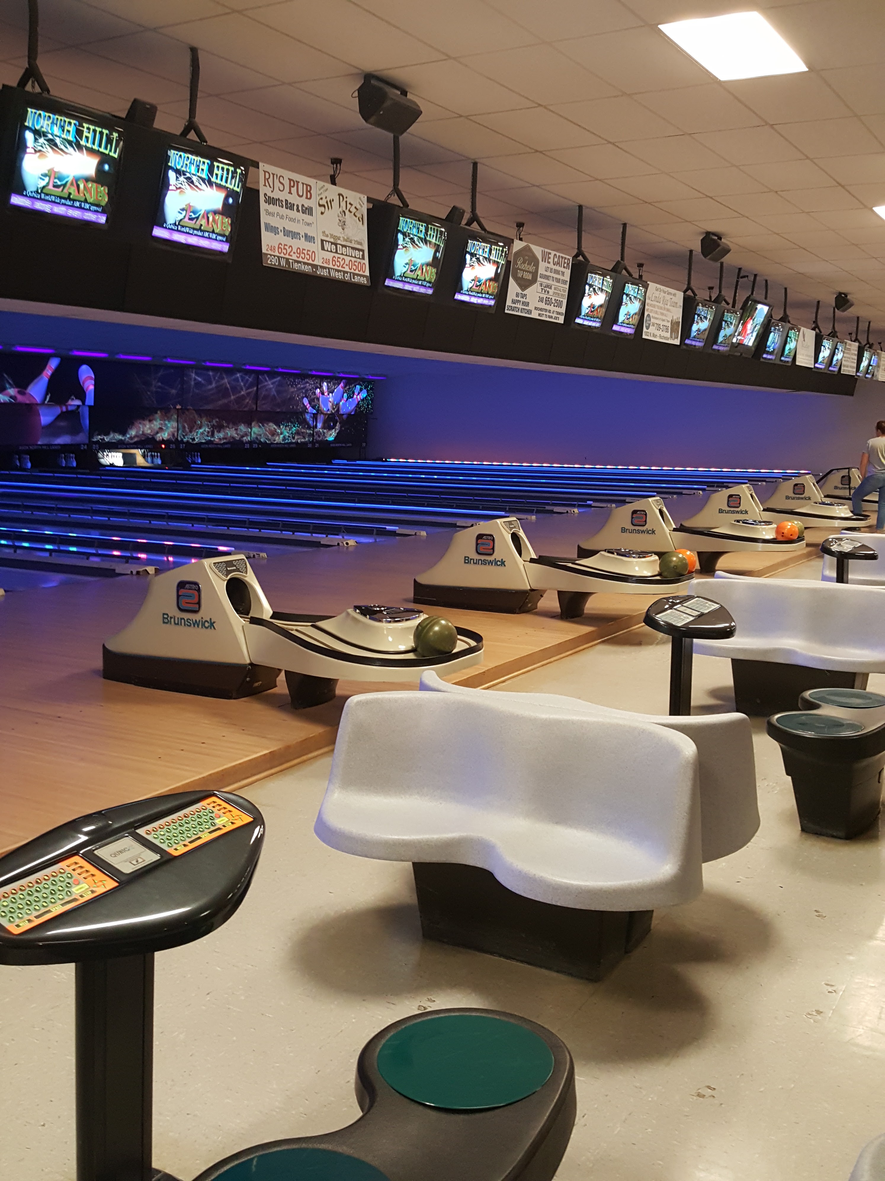 An indoor view of bowling lanes with Brunswick equipment, scoring monitors, and seating areas.