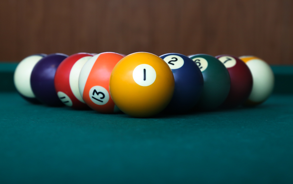 A close-up shot of pool balls arranged on a green billiard table with the yellow 1-ball in sharp focus.