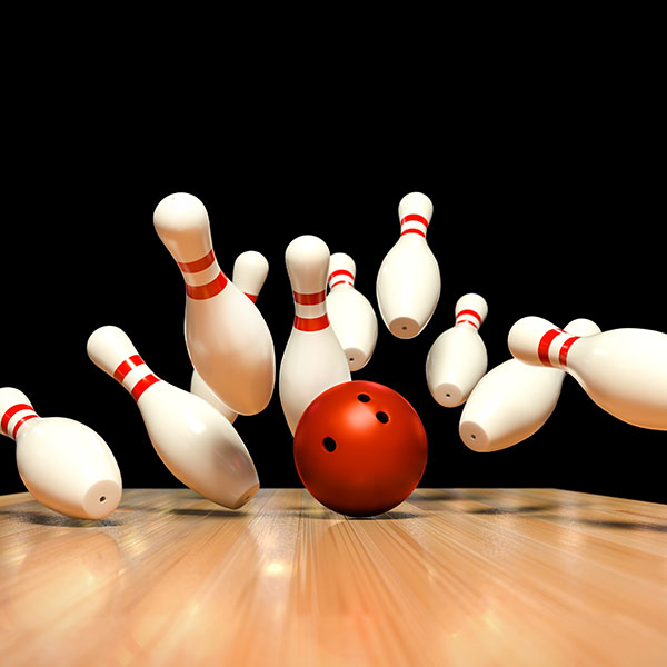 A red bowling ball striking white pins on a wooden lane against a black background.