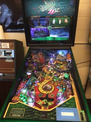 An illuminated Wizard of Oz pinball machine featuring a colorful playfield and a digital backglass screen.