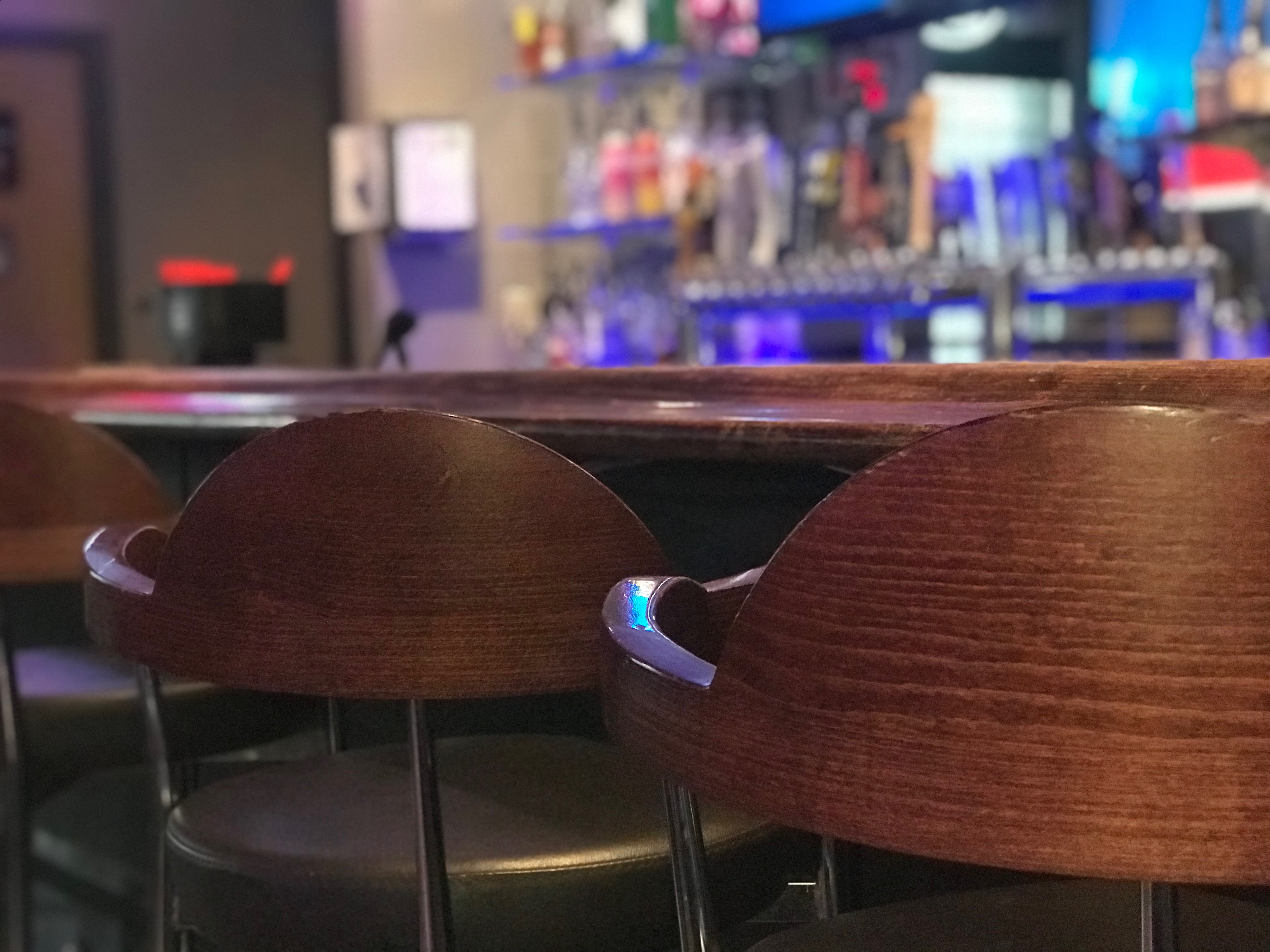 Close-up of wooden bar stools at a bar counter with blurred blue accent lighting in the background.