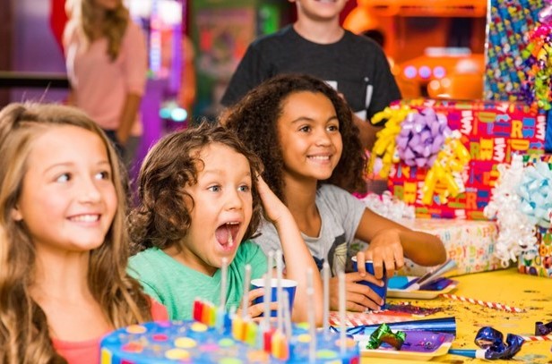 Excited children celebrating a birthday party with a colorful cake and wrapped presents.
