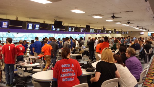 A busy bowling center filled with a large crowd of people in colorful shirts near the lanes.