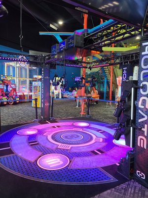 A circular VR gaming platform glows with purple and blue lights inside an arcade.