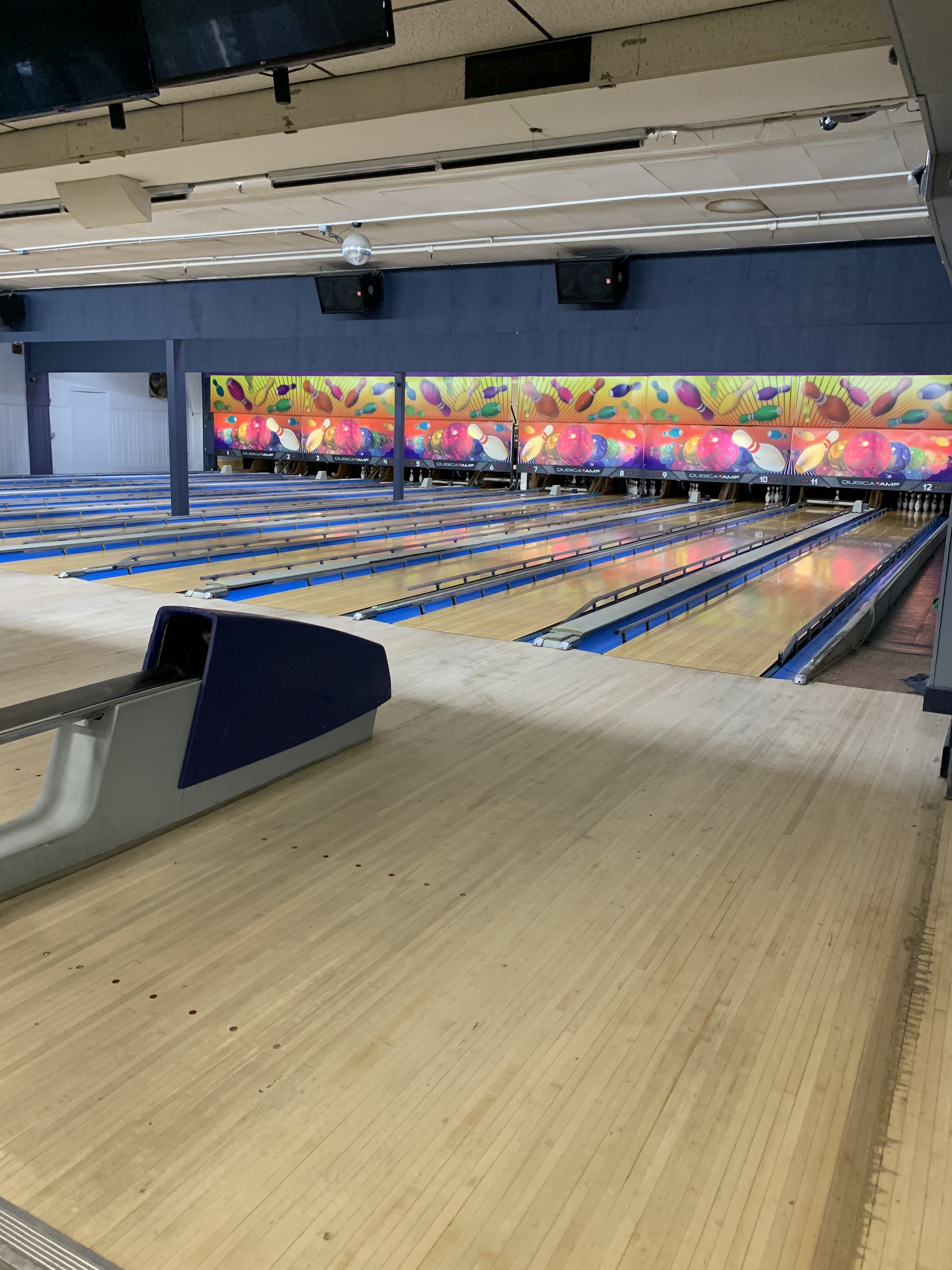 A vertical view of polished wooden bowling lanes with colorful graphics on the back walls.