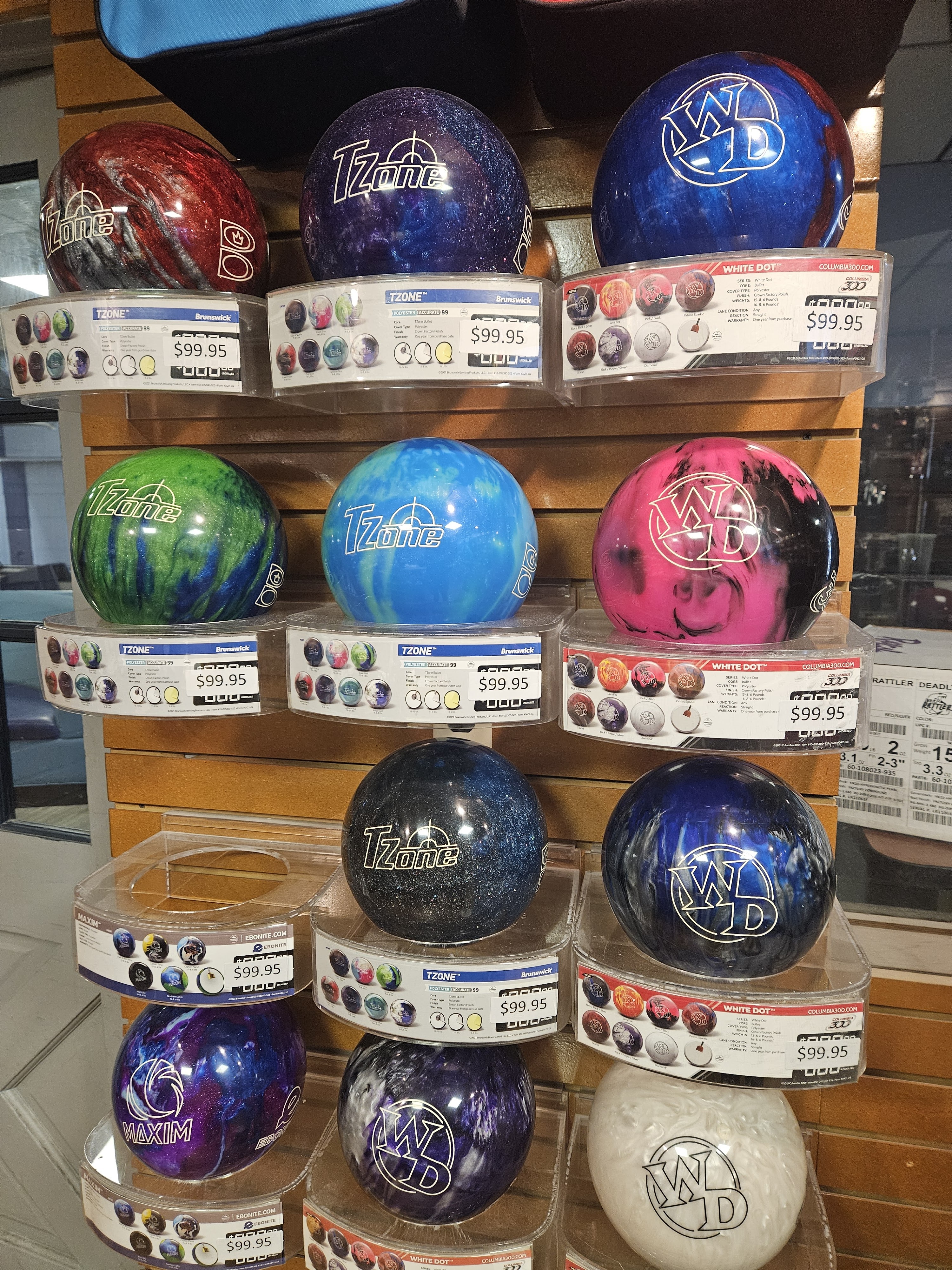 Rows of colorful new bowling balls on clear display stands in a pro shop with price tags.