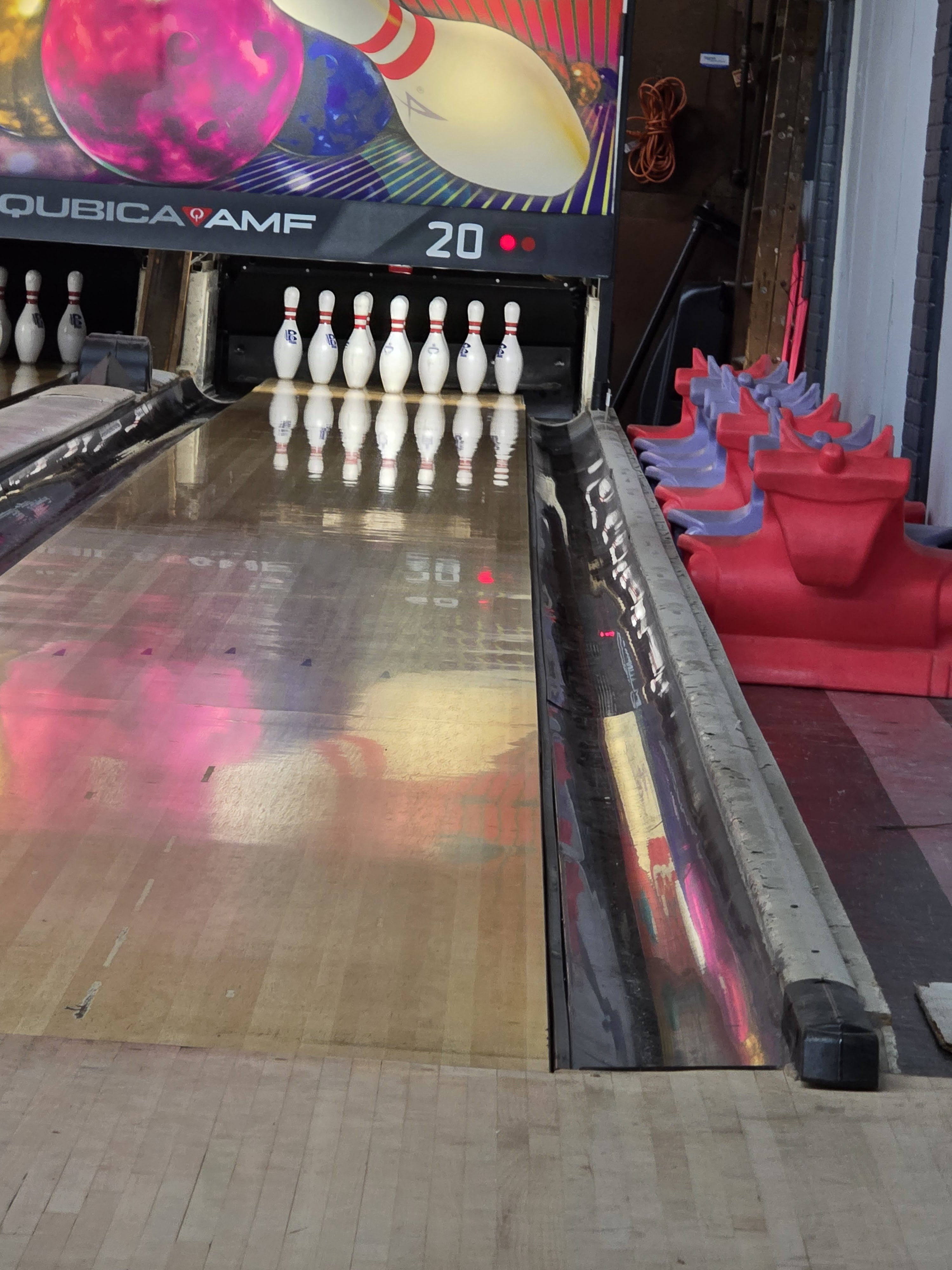 A polished bowling lane set with ten pins and stacked colorful dragon-shaped bowling ramps for kids.