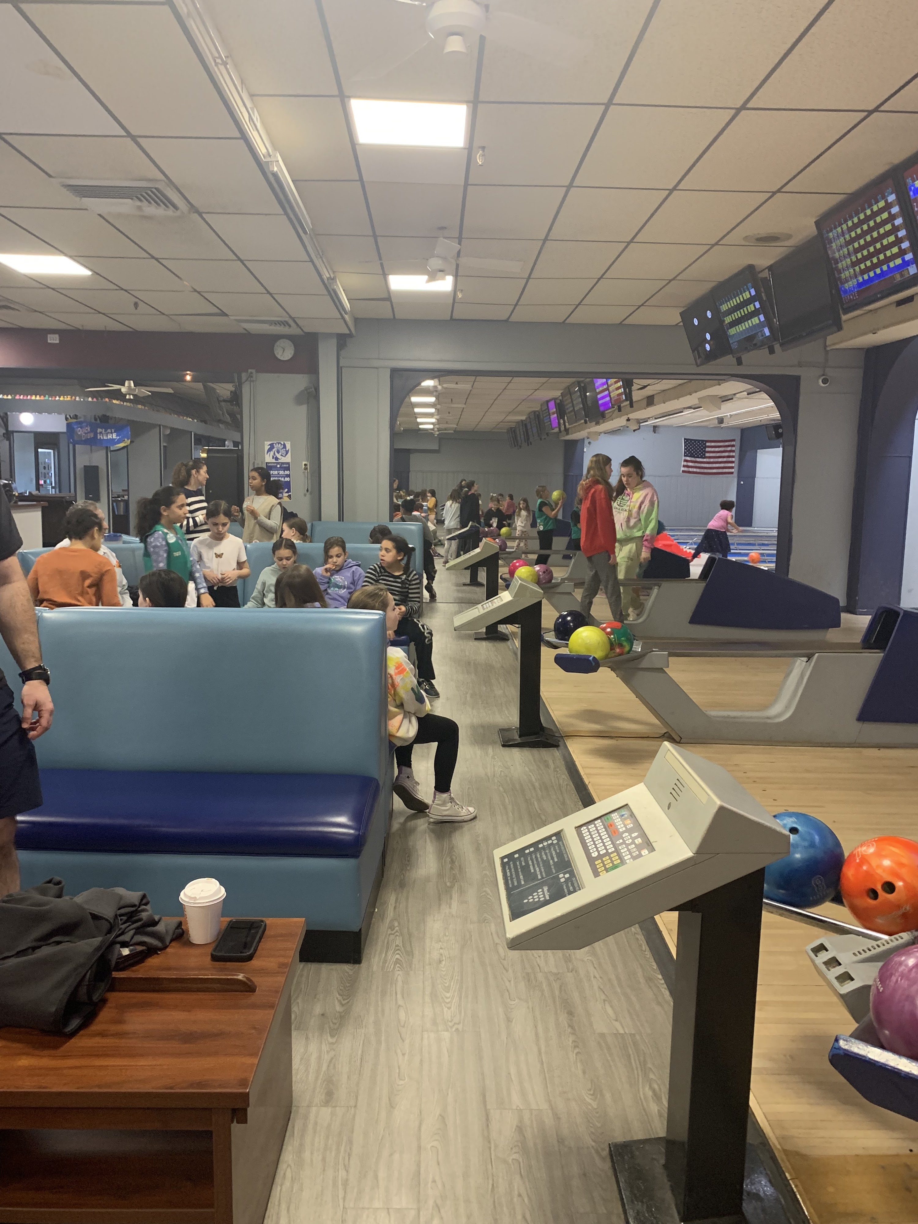 A group of children and teenagers gathering at a bowling center with blue booths and active lanes.