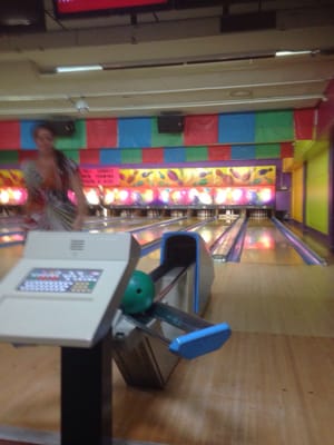 A green bowling ball on a ball return next to a scoring console at a bowling alley.