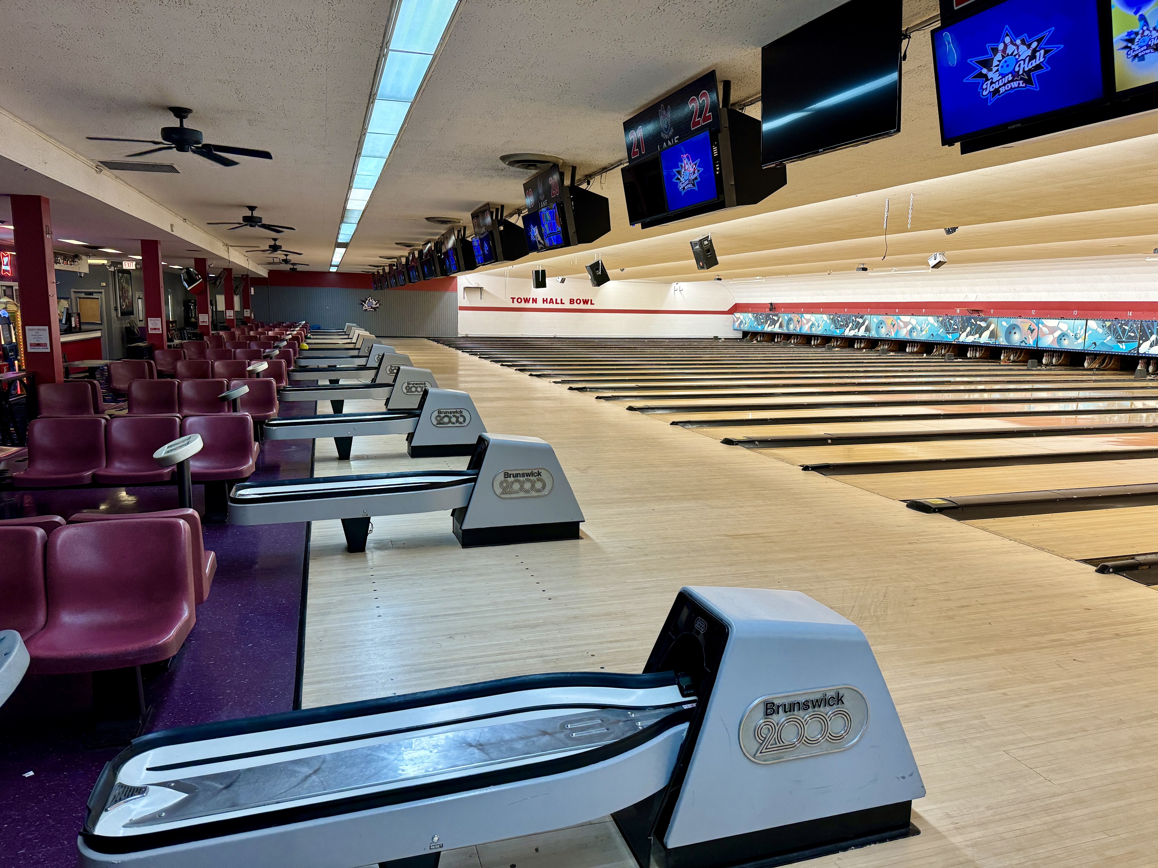 A wide view of multiple bowling lanes and seating area with overhead scoring screens displaying the Town Hall Bowl logo.
