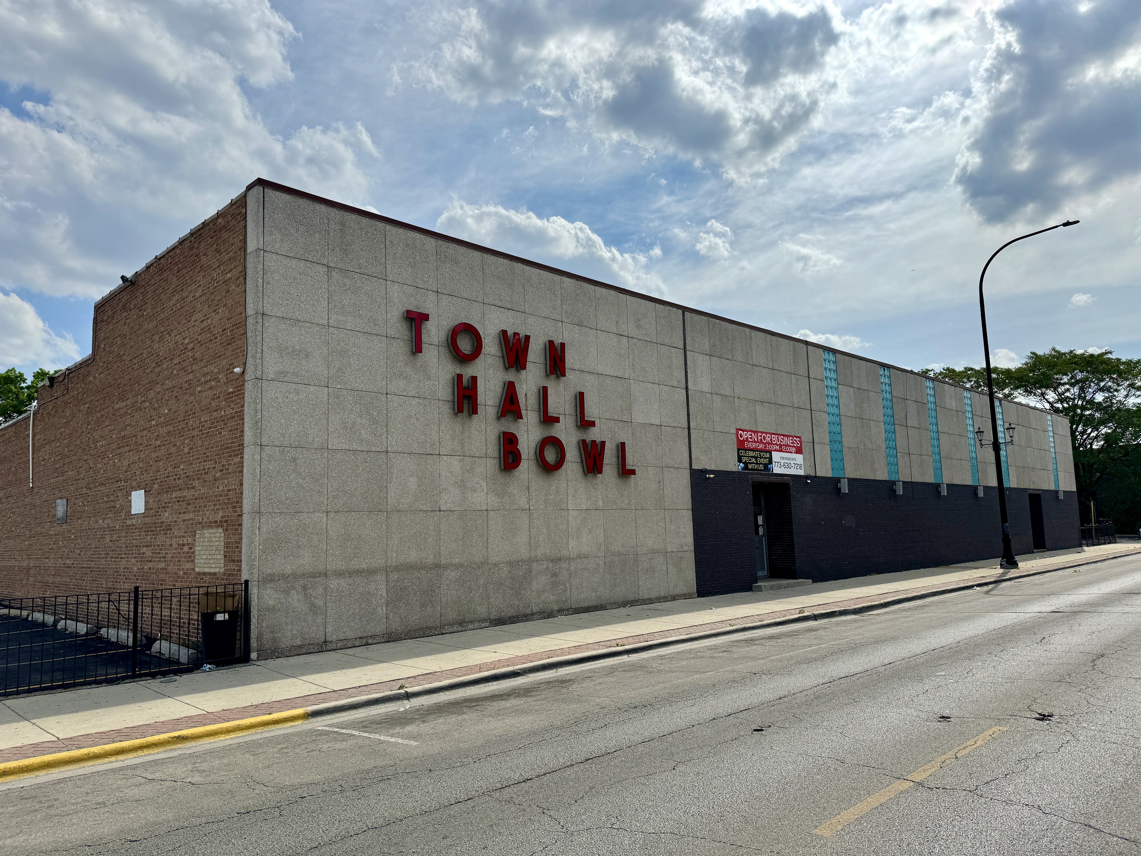 Exterior view of Town Hall Bowl, a large building with red lettering, concrete and brick facade, and an "Open For Business" banner.
