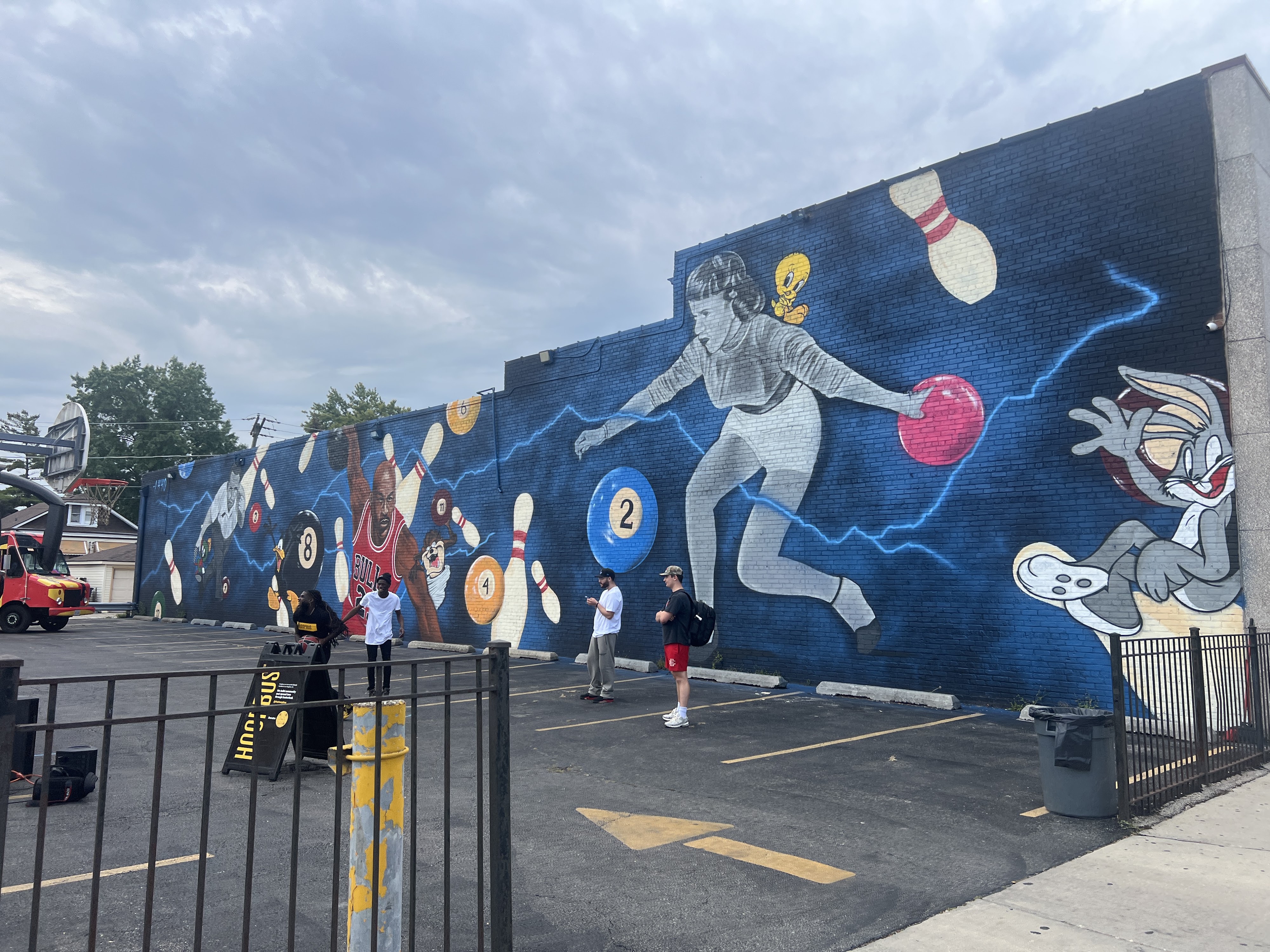 A vibrant mural on a dark blue brick wall depicting bowling, billiards, and popular cartoon characters like Bugs Bunny and Michael Jordan.
