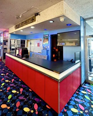 A vibrant red and black service counter with a patterned carpet floor featuring bowling pins and shoe prints.