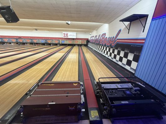 An empty bowling alley with multiple lanes stretching towards the pin decks and a retro-themed wall mural.