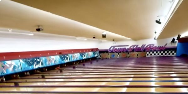 A wide shot of multiple empty bowling lanes at Town Hall Bowl, with the center's logo visible on the back wall.