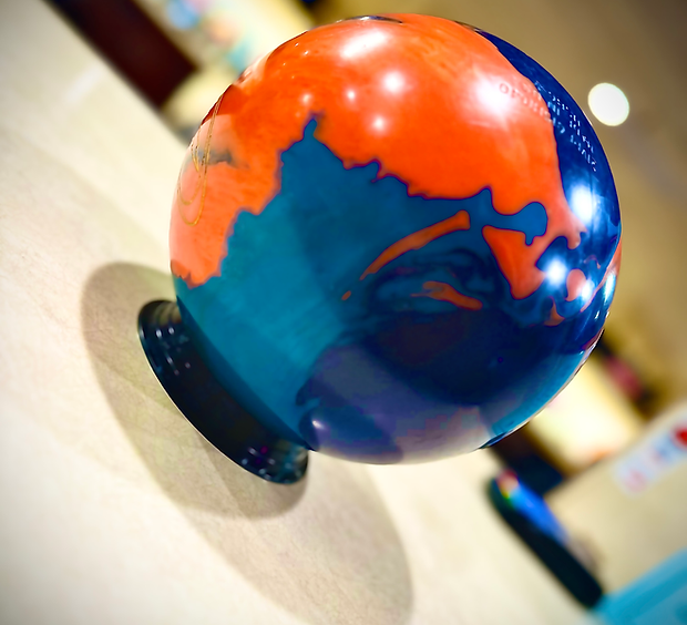 A close-up, angled photo of a blue and orange bowling ball designed to look like the Earth, resting on a ball return.
