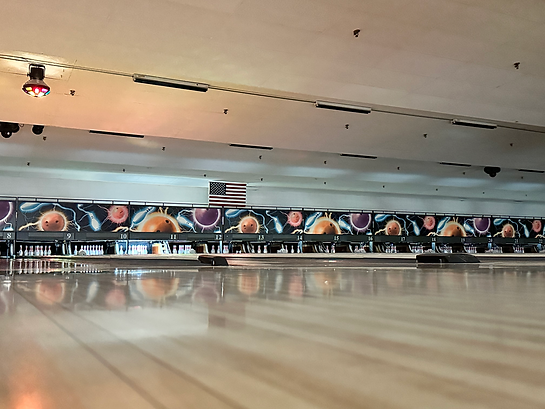 A wide shot of bowling lanes with cosmic-themed graphics above the pins and a disco light hanging from the ceiling.