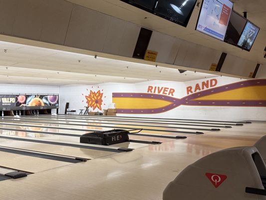 View down a series of bowling lanes towards a colorful mural that reads "River Rand".