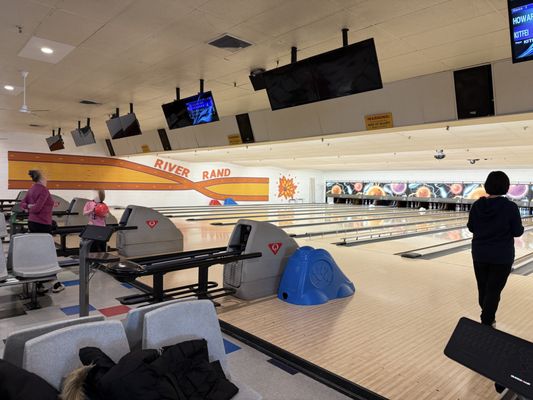View of bowling lanes at River Rand Bowl with several people bowling and automatic scoring screens visible.