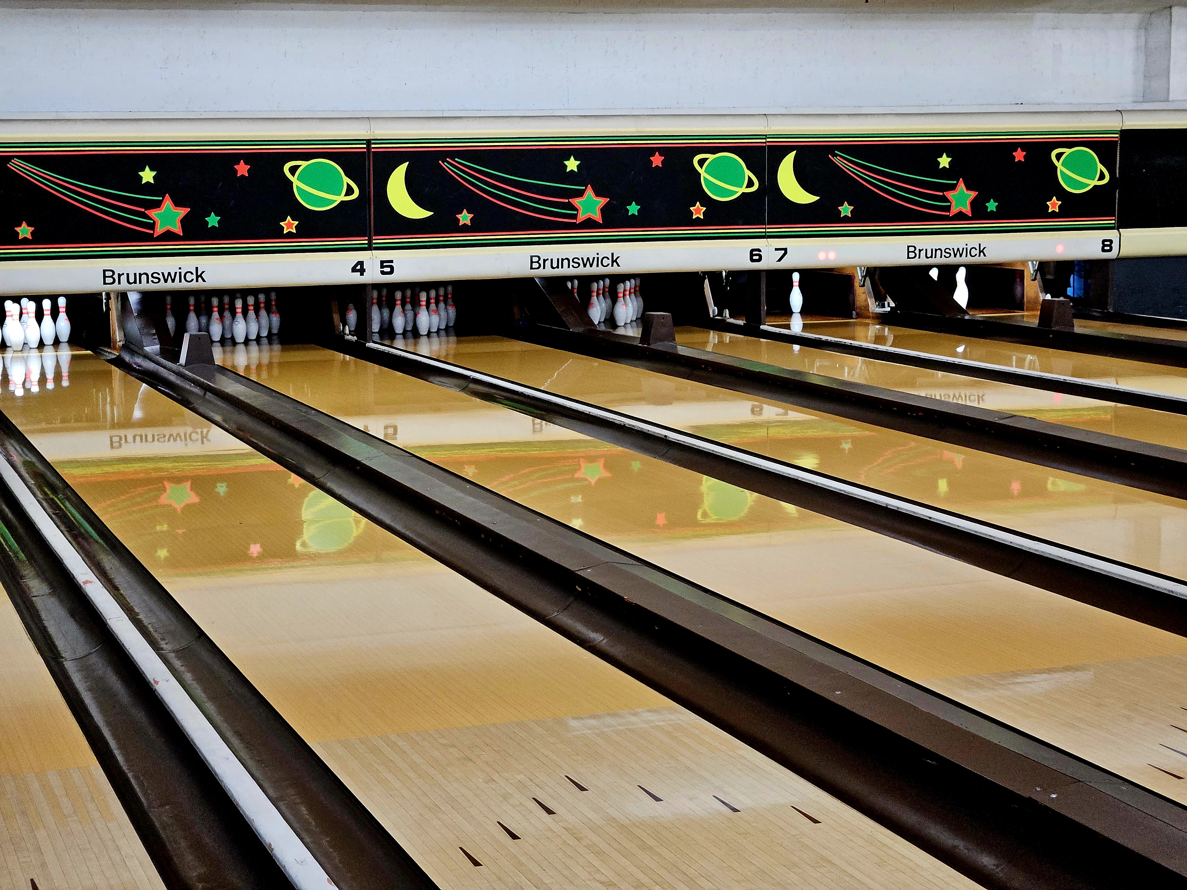 A vibrant overhead view of several bowling lanes with colorful cosmic-themed backdrops and bowling pins set up at the end.