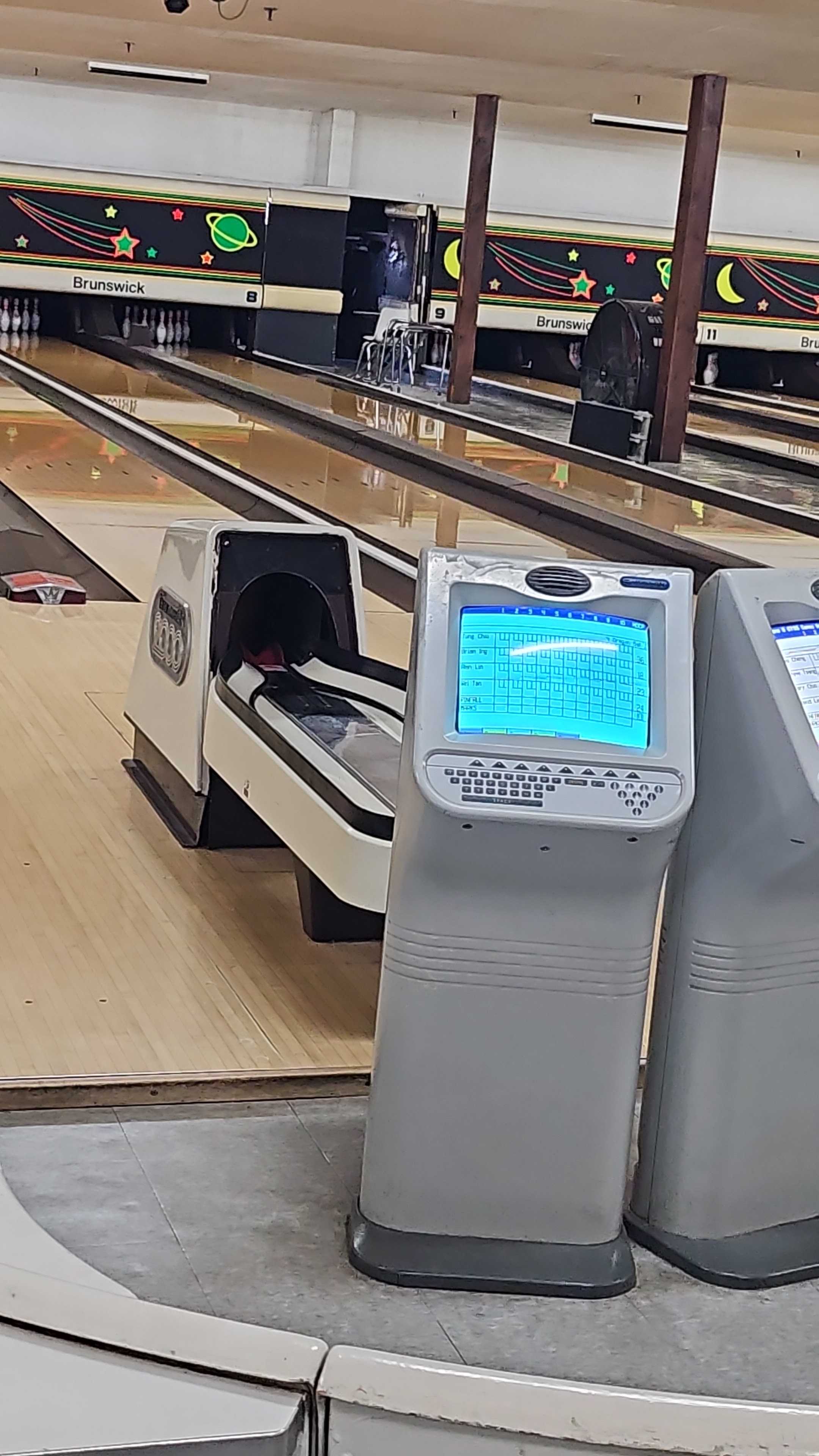 A close-up view of a bowling lane with an automatic scoring screen showing blue text on a grid.