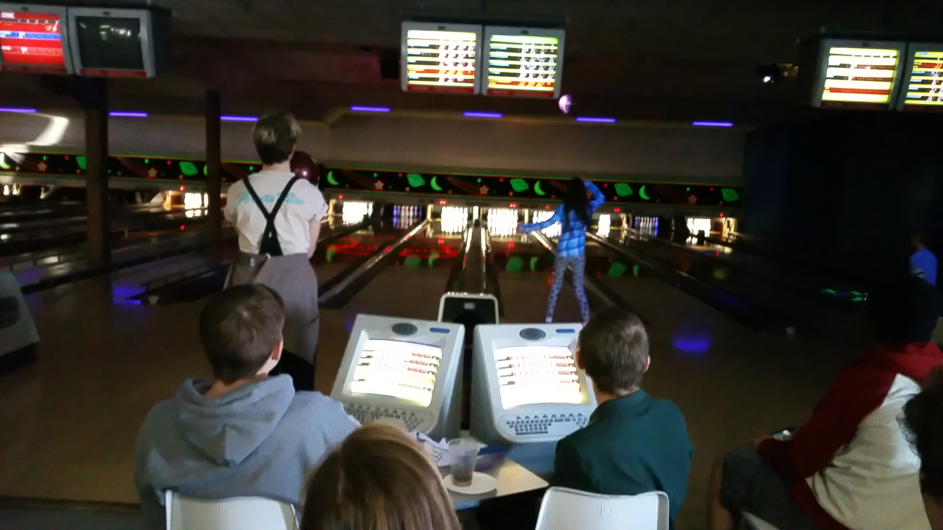 People bowling during a cosmic bowling session with glowing lanes and automatic scoring monitors.