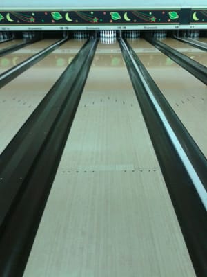 A low-angle shot of multiple bowling lanes leading up to a set of white bowling pins.
