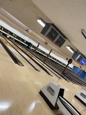 A low, angled view of multiple bowling lanes with ball returns and automatic scoring monitors visible.