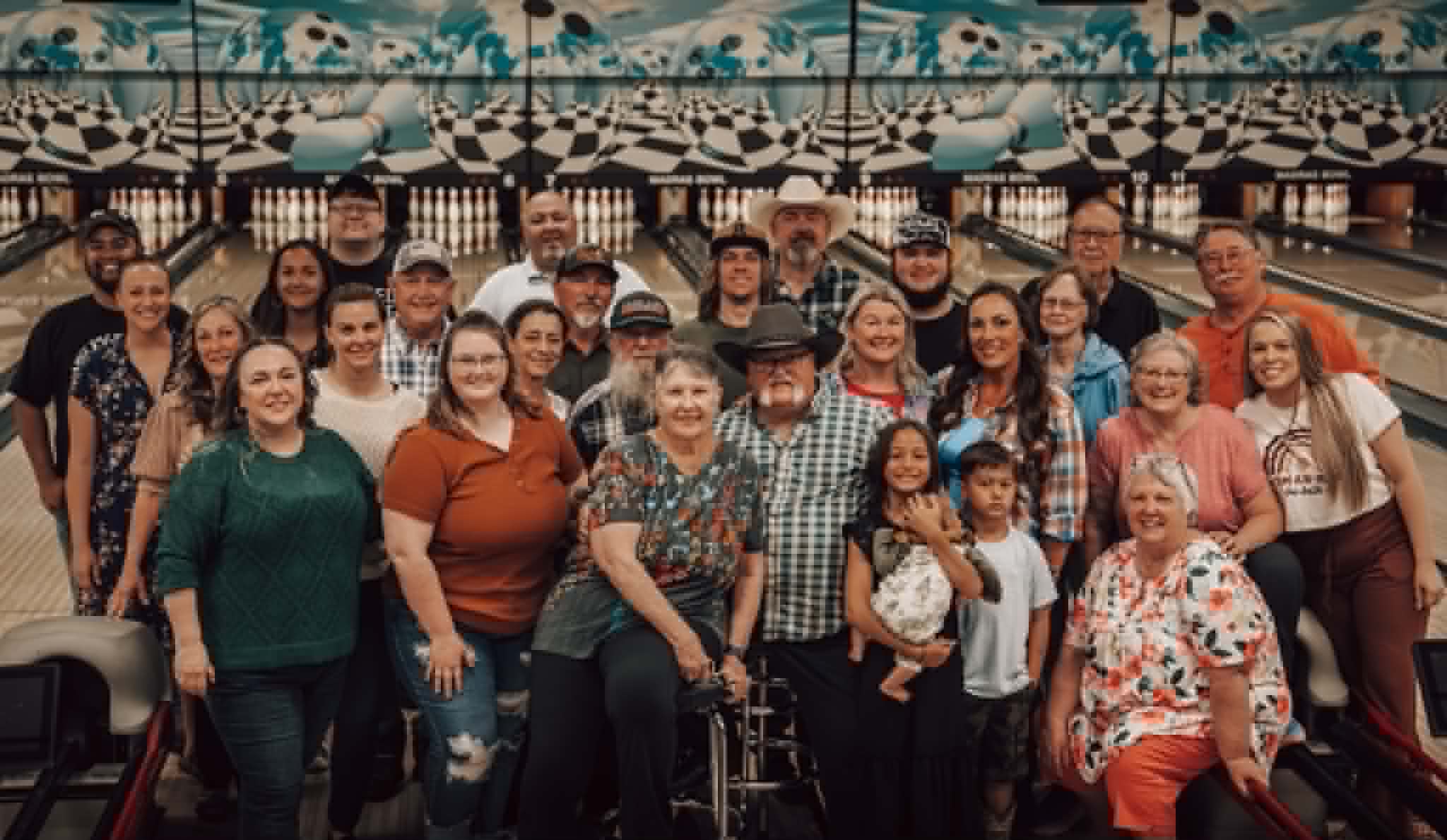 A large multi-generational group of people smiling and posing for a photo on the bowling lanes.